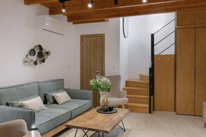 Ein Wohnzimmer mit grauem Sofa, einem Holztisch und einer Holztreppe, die zu einer Holztür führt.