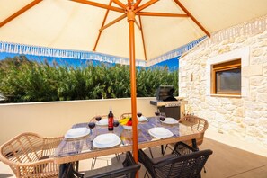 An outdoor dining area with a table set for four, a grill, and a stone wall backdrop. - Villa Filio - Two Bedroom Villa, Sleeps 4 (Adele)