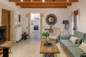 A living room with a wooden ceiling, a sofa, a coffee table, a TV, and a kitchen in the background. - Villa Filio - Two Bedroom Villa, Sleeps 4 (Adele)