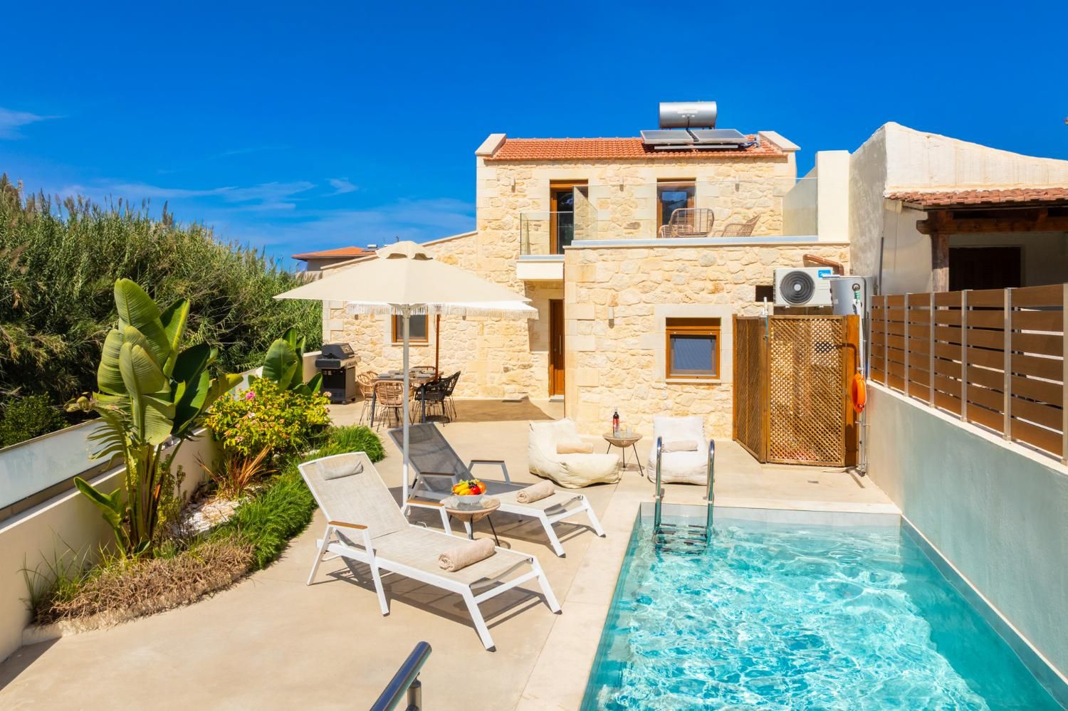 A poolside area with lounge chairs, a table with fruit, and a stone building with a tiled roof.