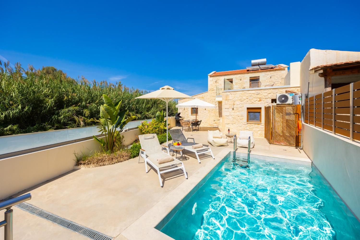 Ein Pool mit Liegestühlen, ein Steinhaus und üppiges Grün.