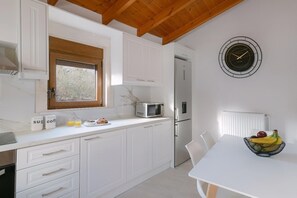 Eine Küche mit weißen Schränken, einer Mikrowelle, einem Kühlschrank, einer Wanduhr und einem Tisch mit Obst.