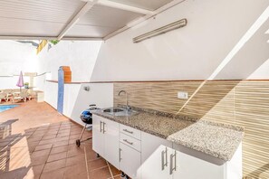 Eine kleine Küche mit Spüle, Arbeitsfläche und Schränken, angrenzend an eine Terrasse mit Schwimmbecken.
