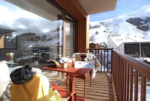 Un balcon doté d’un plancher en bois, une table avec une chaise, et une vue sur un paysage montagneux enneigé.