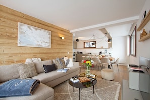 A modern living room with a sofa, coffee table, and a dining area with chairs. - Super Venosc | T3 à 100m des pistes, 50m télésiège (MONT-DE-LANS)