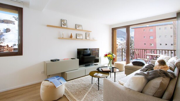 Ein modernes Wohnzimmer mit Fernseher, Sofa und einem Balkon mit Blick auf ein Gebäude.