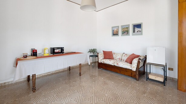 A room with a dining table, a sofa, a lamp, and a wall with three framed pictures. - Apartment 'Alle Colonne Bianche Rooms' with Balcony, Wi-Fi and Air Conditioning (Conversano)