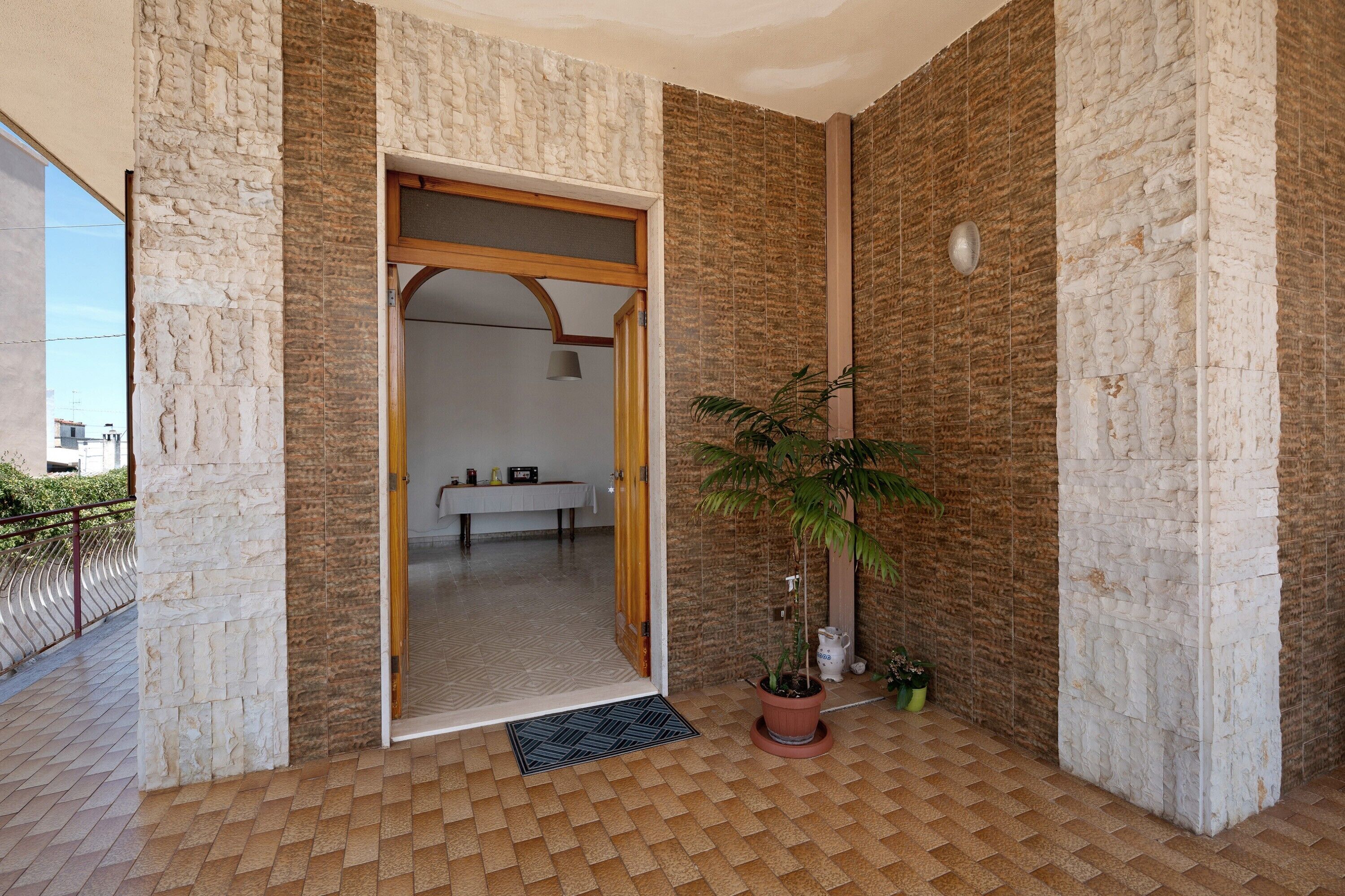 Quarto com parede de pedra, porta de madeira, planta em vaso e piso de azulejos.