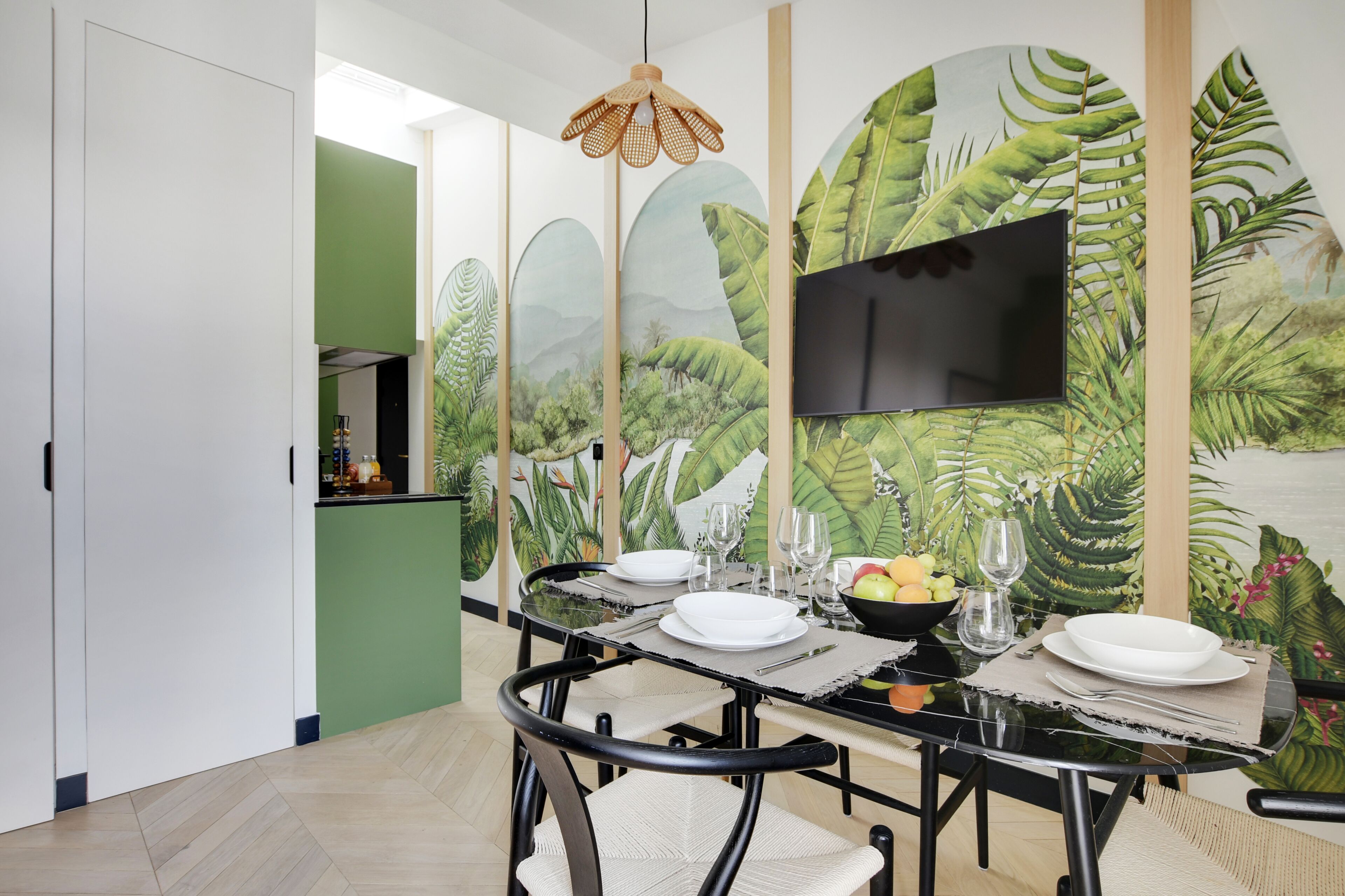 Ein Essbereich mit einem Tisch für vier Personen, einem an der Wand montierten Flachbildfernseher und einer Wandmalerei von tropischer Vegetation.