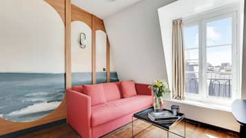 Uma sala de estar moderna com um sofá vermelho, uma mesa de centro com livros, um mural na parede e uma janela com vista para a cidade.