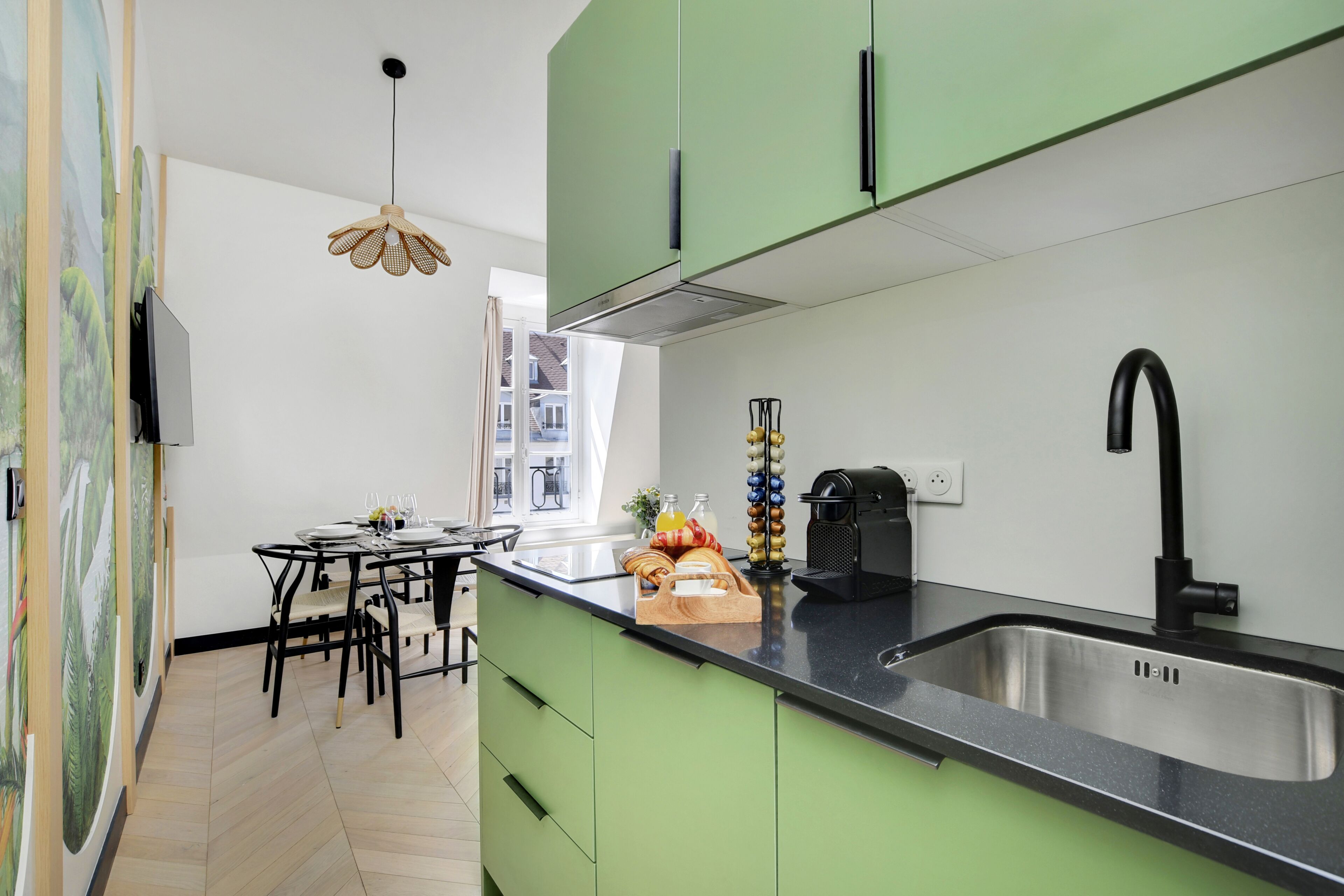 Una cocina moderna con armarios verdes, un lavamanos de acero inoxidable y una zona de comedor con mesa y sillas.