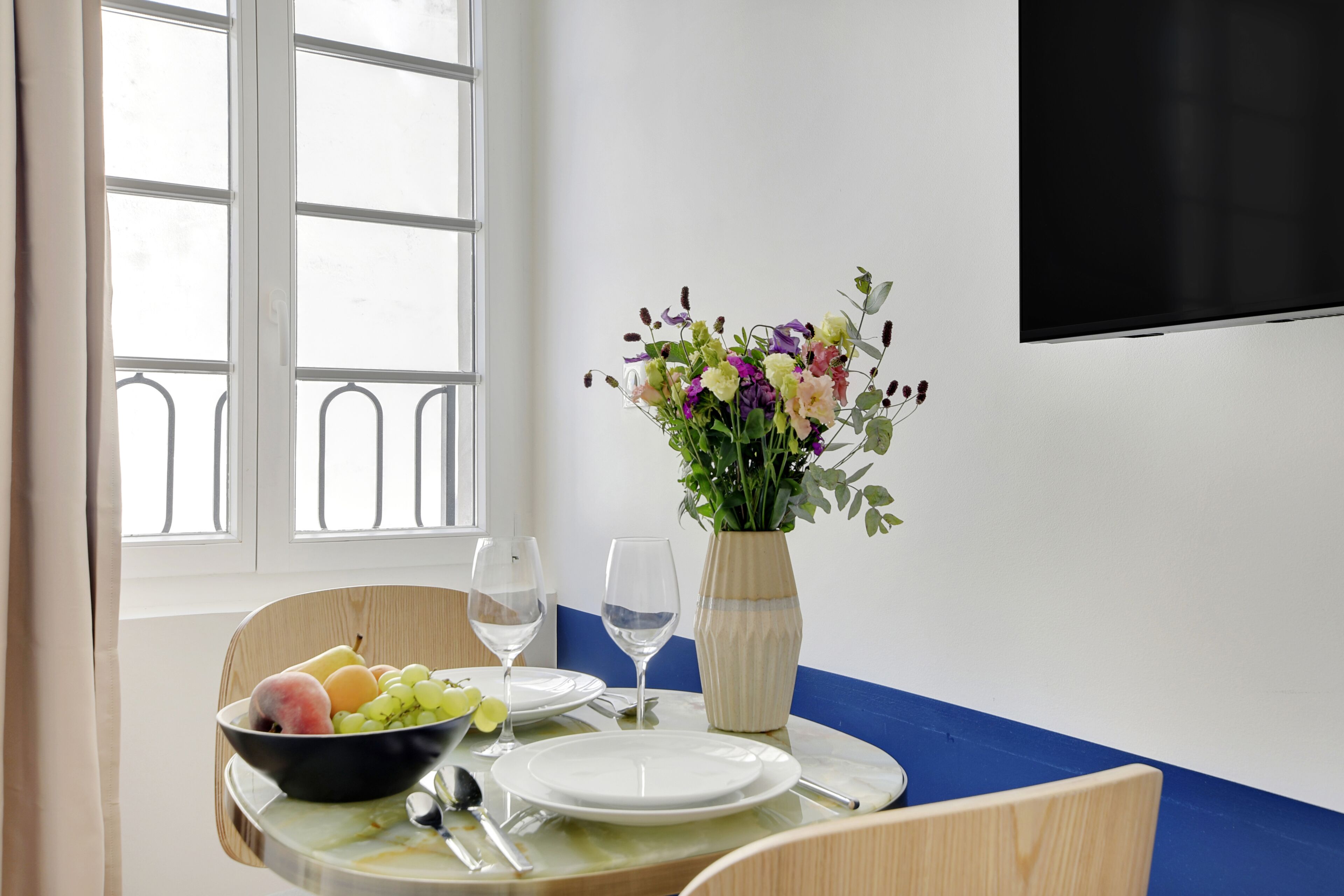 A dining table with a bowl of fruit, a vase of flowers, and a wine glass.