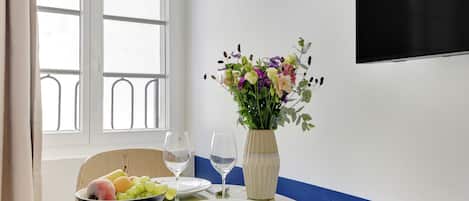 Une table à manger avec un saladier de fruits, un vase de fleurs et un verre à vin.
