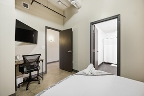 Ein Hotelzimmer mit einem Bett, einem Schreibtisch mit Stuhl, einem Spiegel, einem Fernseher und einer Tür zu einem Badezimmer.
