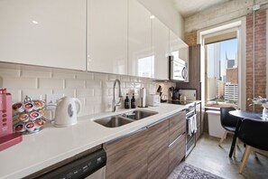 Eine moderne Küche mit weißen Schränken, Edelstahlgeräten und Blick auf die Stadt durch ein großes Fenster.