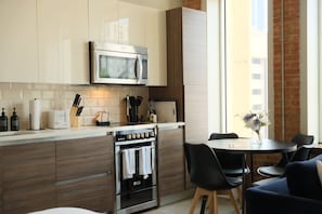 A modern kitchen with a built-in microwave, oven, and a dining area with a table and chairs. - Stylish Downtown Stay | Pool, Gym, Valet Parking (Dallas)