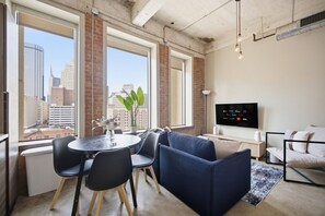 Ein modernes Wohnzimmer mit großem Fenster, einer Couch, einem Fernseher und einem Essbereich mit Stühlen.