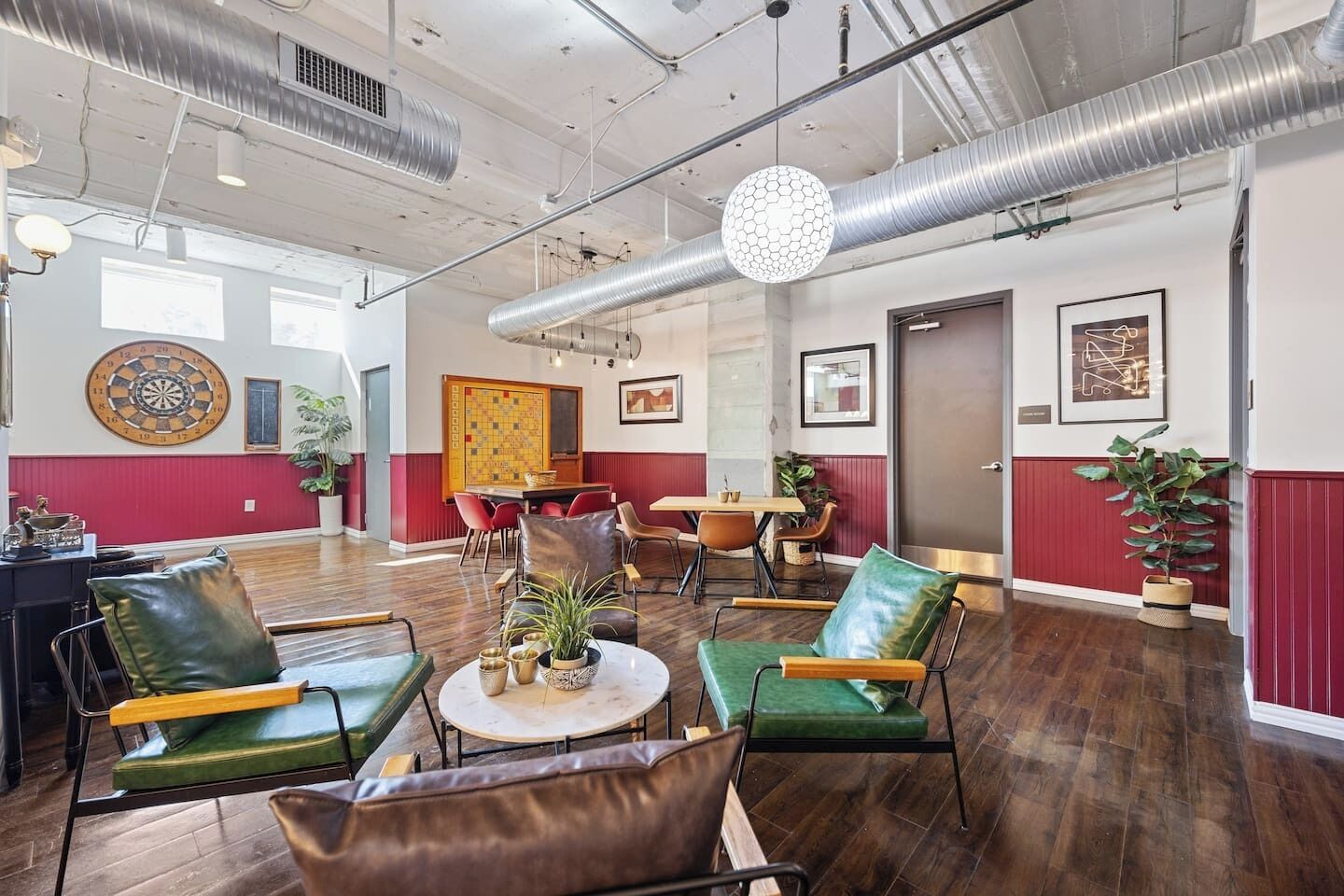 A spacious room with a dartboard, a table with chairs, and a large window.