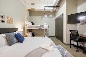 Een hotelkamer met een stapelbed, een bureau met stoel, een televisie en een kledingkast.