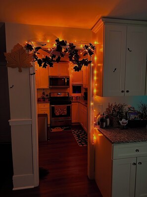 A kitchen with white cabinets, a microwave, and a stove. There are decorative lights and a Halloween-themed rug. - The Salem Spookhouse 3BR with Free Parking! Sleeps 8! (Salem)