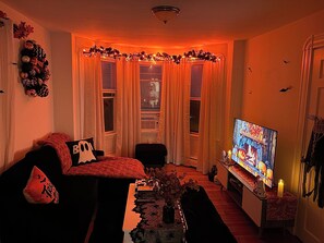 A living room with a television, a sofa, a coffee table, and a decorative plant. - The Salem Spookhouse 3BR with Free Parking! Sleeps 8! (Salem)