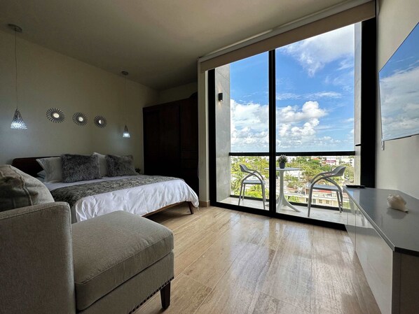 A bedroom with a bed, a chair, a balcony with a view, and a desk. - Musa del Carmen · Partial Ocean View & Rooftop+Gym (Playa del Carmen)