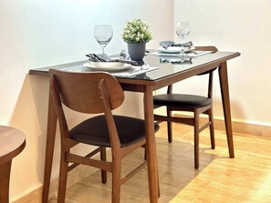 A dining table with two chairs, a potted plant, and two wine glasses. - Musa del Carmen · Partial Ocean View & Rooftop+Gym (Playa del Carmen)
