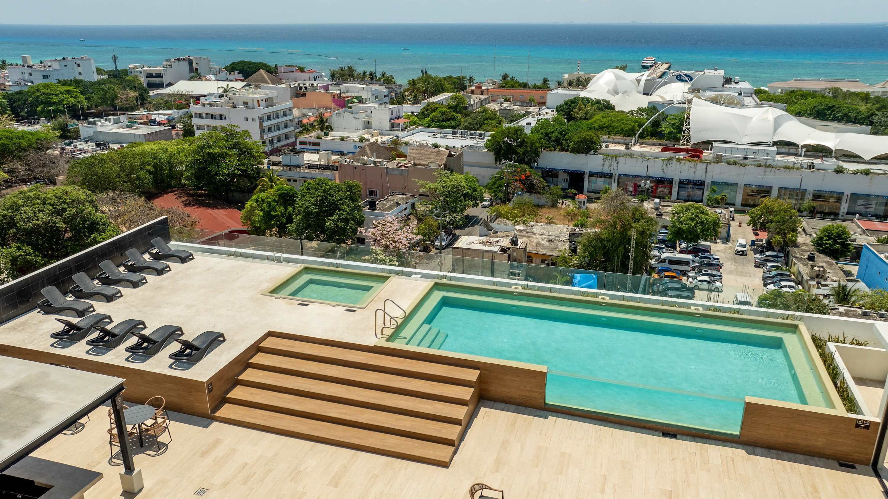 A rooftop pool with lounge chairs and a view of the ocean.