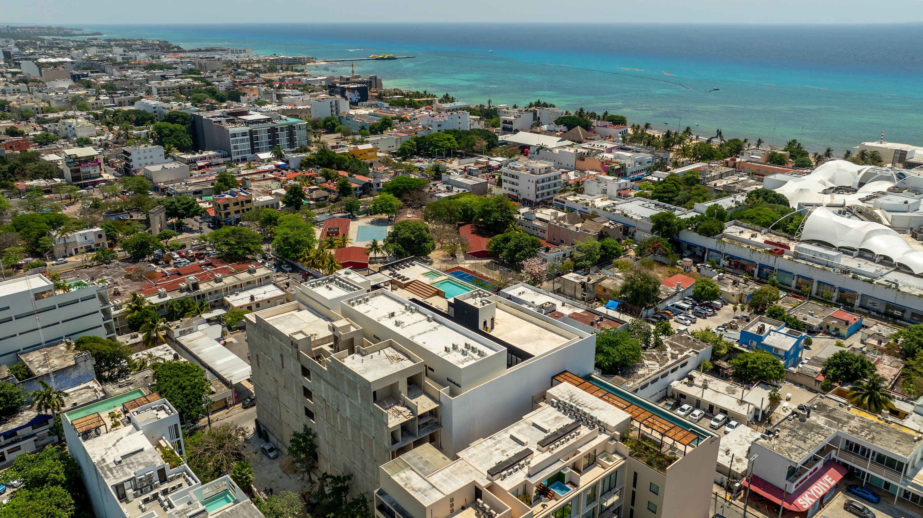 A coastal cityscape with dense urban development, a prominent pool area, and a clear view of the ocean.