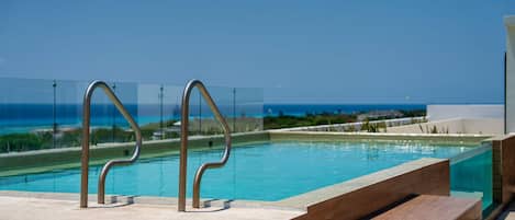 A clear blue sky, a swimming pool with metal poolside steps, and a view of the ocean.