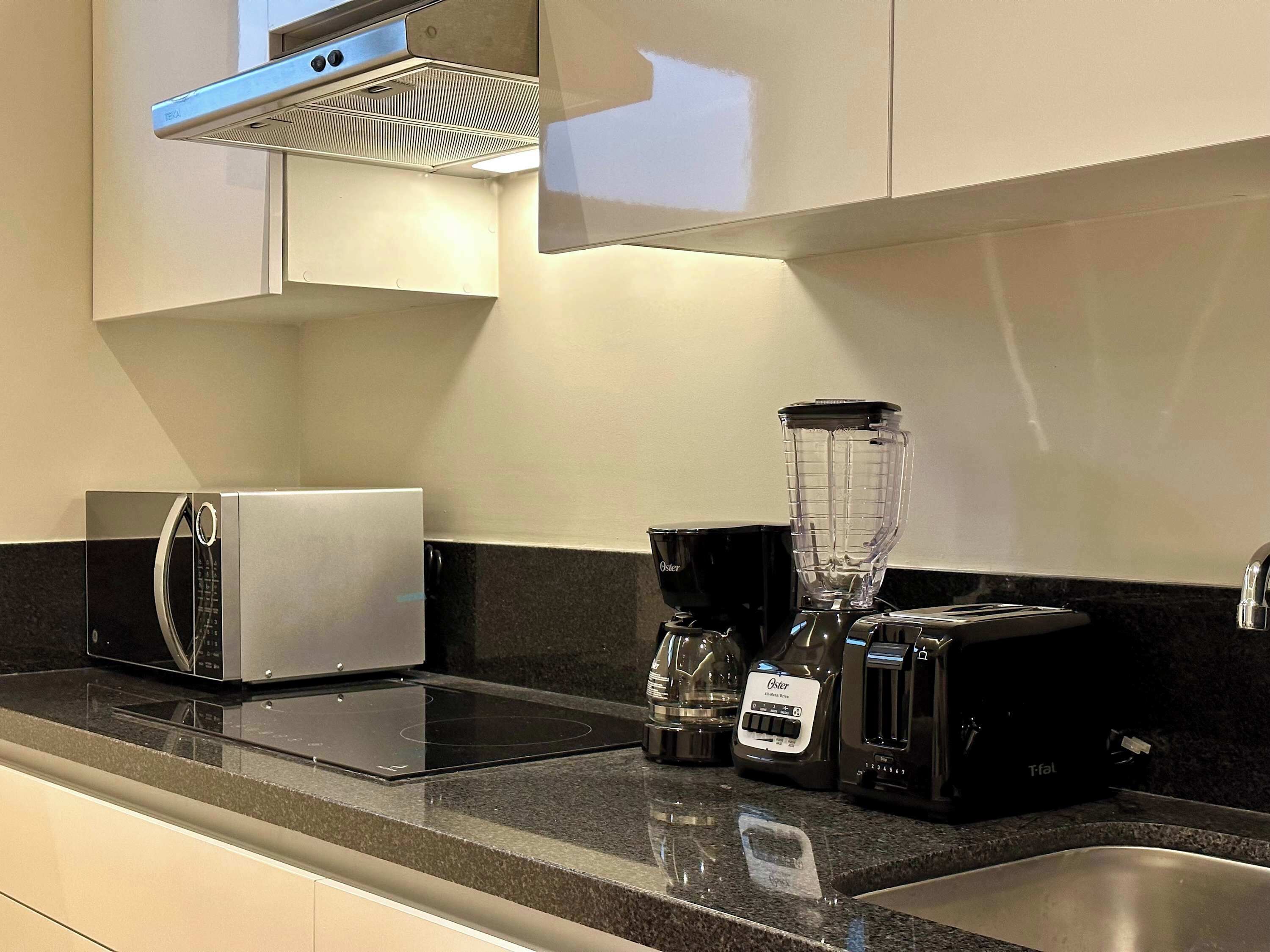 Une cuisine moderne équipée d’un grille-pain encastré, d’un mixeur et d’une machine à café, le tout posé sur un plan de travail en granit.