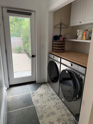 A laundry room with a washing machine, dryer, and a small shelf with cleaning products. - Welcome to The Springs House, a beautiful home in a peaceful neighborhood. (East Hampton)