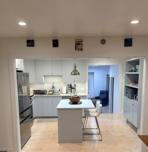 A modern kitchen with white cabinets, a central island, and a dining area with a chair. - Welcome to The Springs House, a beautiful home in a peaceful neighborhood. (East Hampton)