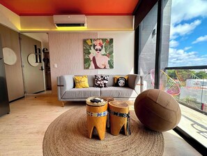 A modern living room with a grey sofa, patterned cushions, a round woven rug, and a large round object. - Musa del Carmen · Frida Style 1BR w/ Pool & Gym (Playa del Carmen)