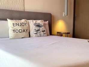 A neatly made bed with two pillows, one with 'ENJOY TODAY' and the other with a mushroom design. - Musa del Carmen · Frida Style 1BR w/ Pool & Gym (Playa del Carmen)