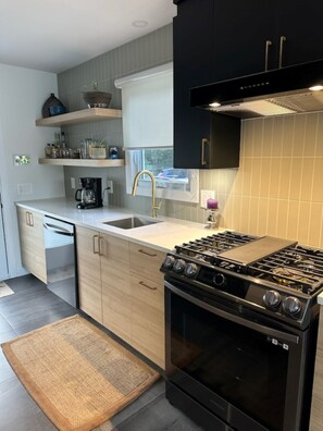 A modern kitchen with a gas stove, dishwasher, and a window above the sink. - A little paradise for all seasons on the shores of Lake St-Alexis (Saint-Alexis-des-Monts)