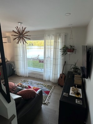 Uma sala de estar com sofá, planta pendente, um violão e uma janela com cortinas.