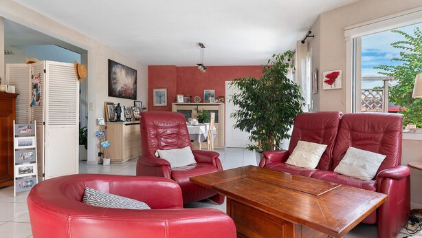 A spacious living room with red leather furniture, a wooden coffee table, and a large window offering a view of the outdoors.
