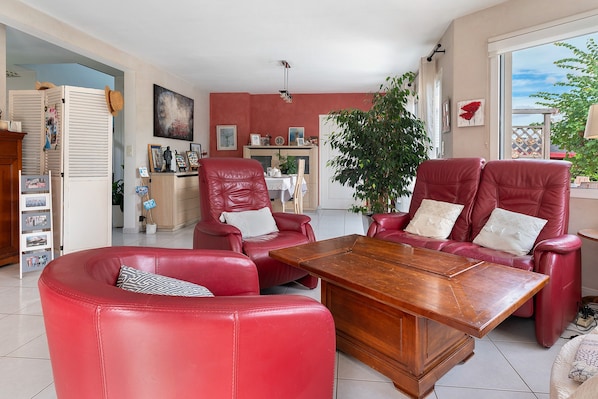 A spacious living room with red leather furniture, a wooden coffee table, and a large window offering a view of the outdoors.