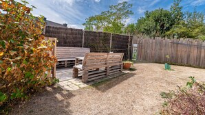 A wooden bench and a table in a backyard with a thatched wall and a wooden fence.