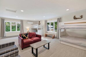 A room with bunk beds, a red leather sofa, a small table, and a window with curtains. - Renovated Door County Bluff Home Panoramic Water Views 4BR Fire pit Sleeps 12 (Sturgeon Bay)