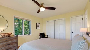 Ein Schlafzimmer mit Bett, Kommode, Stuhl, Deckenventilator, Fenster und Tür.
