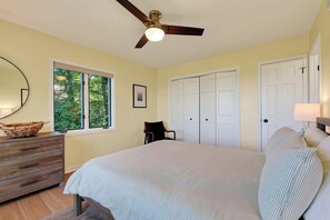 Ein Schlafzimmer mit Bett, Kommode, Stuhl, Deckenventilator, Fenster und Tür.