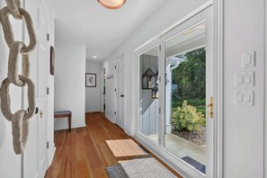 A hallway with a wooden floor, white walls, and a glass door leading to a garden. - Renovated Door County Bluff Home Panoramic Water Views 4BR Fire pit Sleeps 12 (Sturgeon Bay)