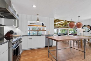 Une cuisine moderne avec des meubles blancs, un îlot central et une vue sur l’extérieur.
