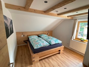 Un dormitorio con cama de madera, ventana con vistas y radiador.