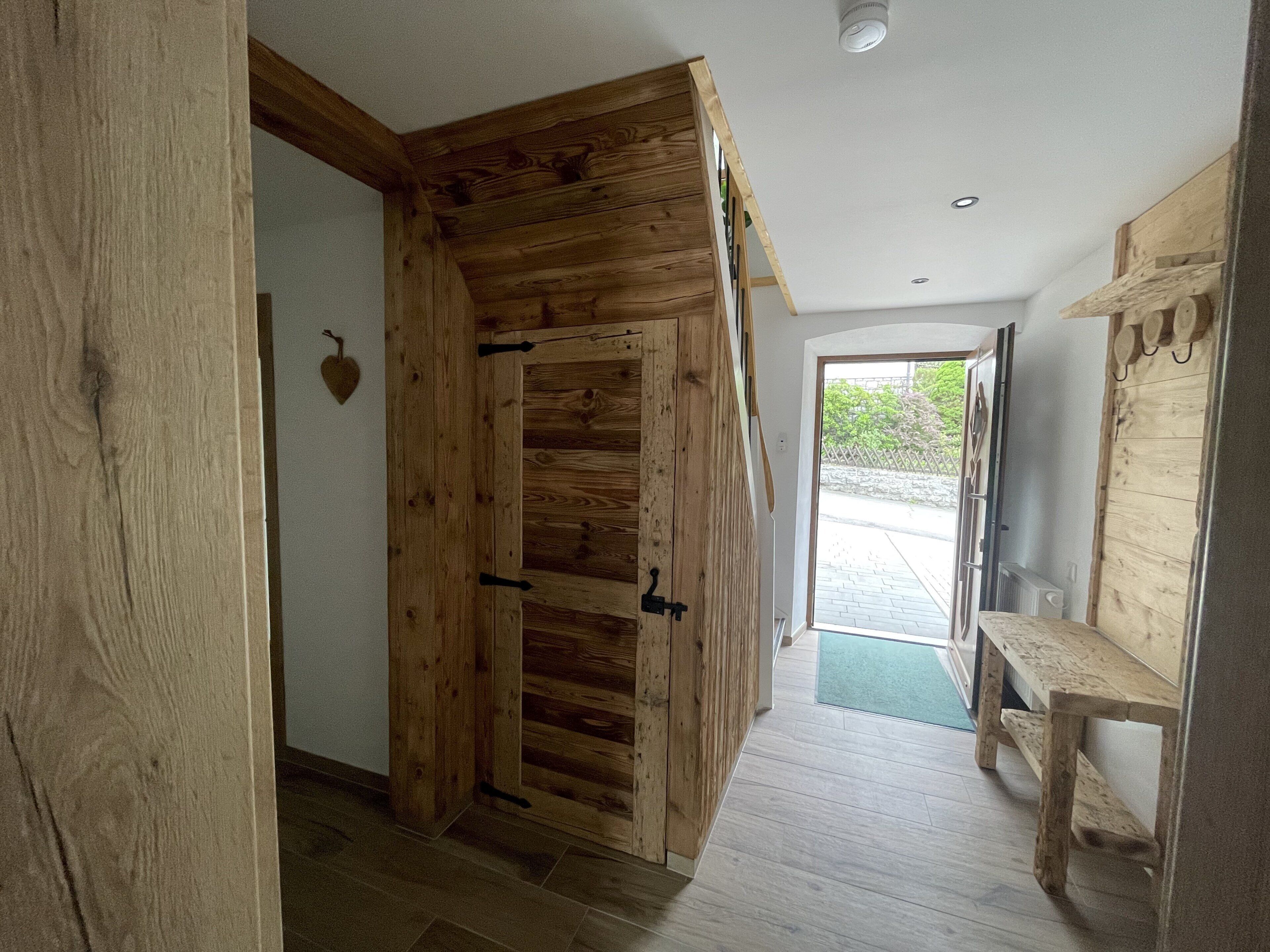 A wooden interior hallway with a door, a bench, and a view to the outside.