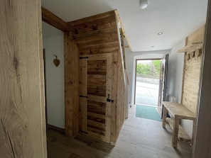 Un pasillo interior de madera con una puerta, un banco y vistas al exterior.