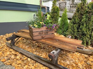 A wooden bench with a planter box labeled "FRUIT FARMS" on a bed of wood chips, surrounded by greenery. - 5-star (DTV) vacation home with plenty of space, a patio, and a fenced-in yard (Wallenfels)