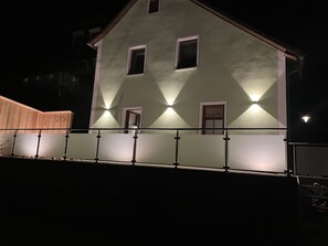 Rakennuksessa on parveke ja useita ikkunoita, ja se on valaistu ulkopuolelta.